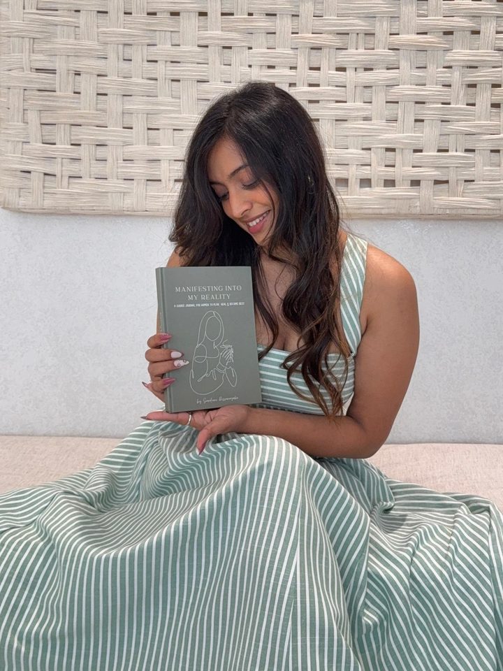 Sanduni Dissanayake, founder of Manifest with Luna, smiling and holding her journal